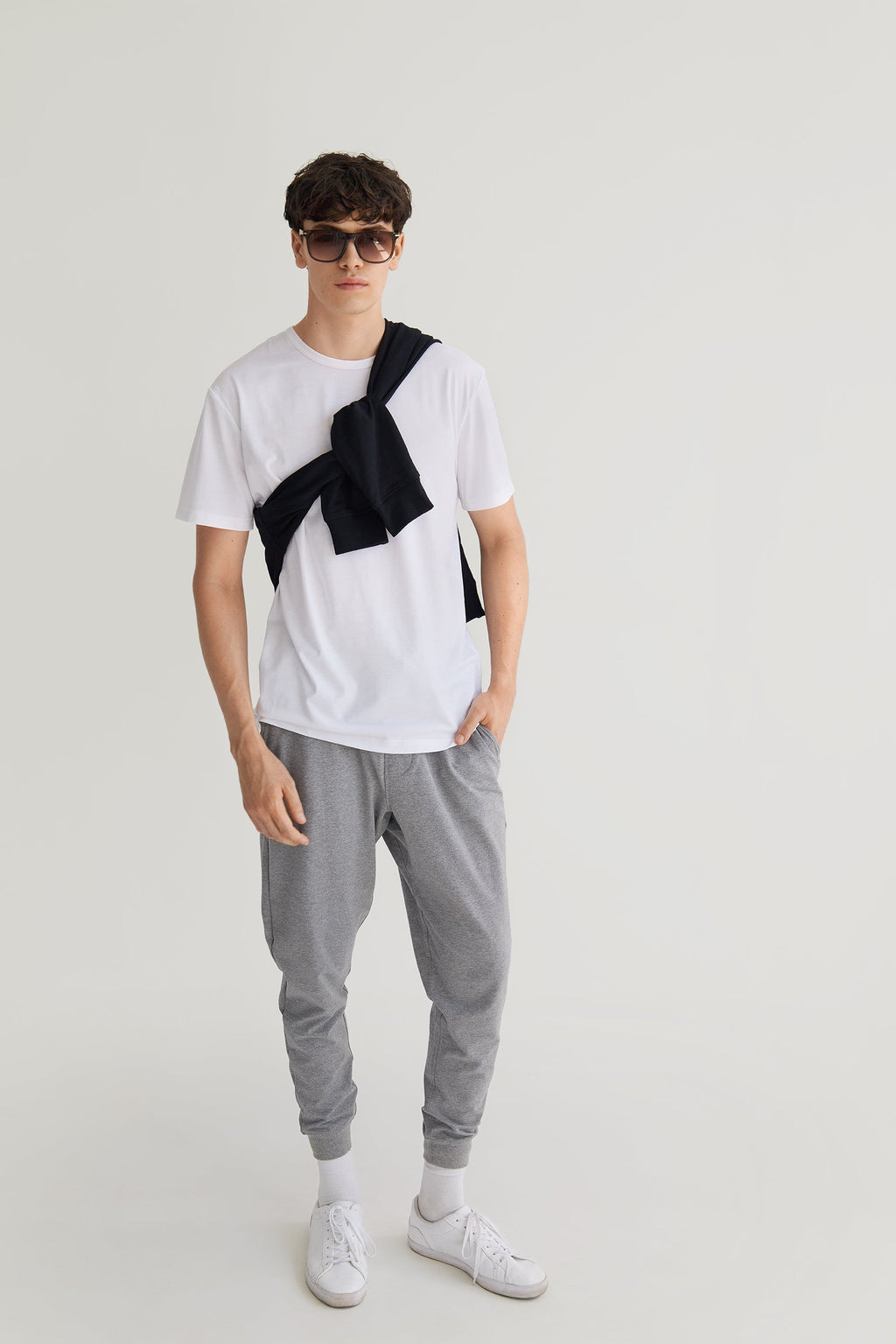 Person wearing a white t-shirt with black suspenders, gray jogger pants, and white sneakers on a light gray background