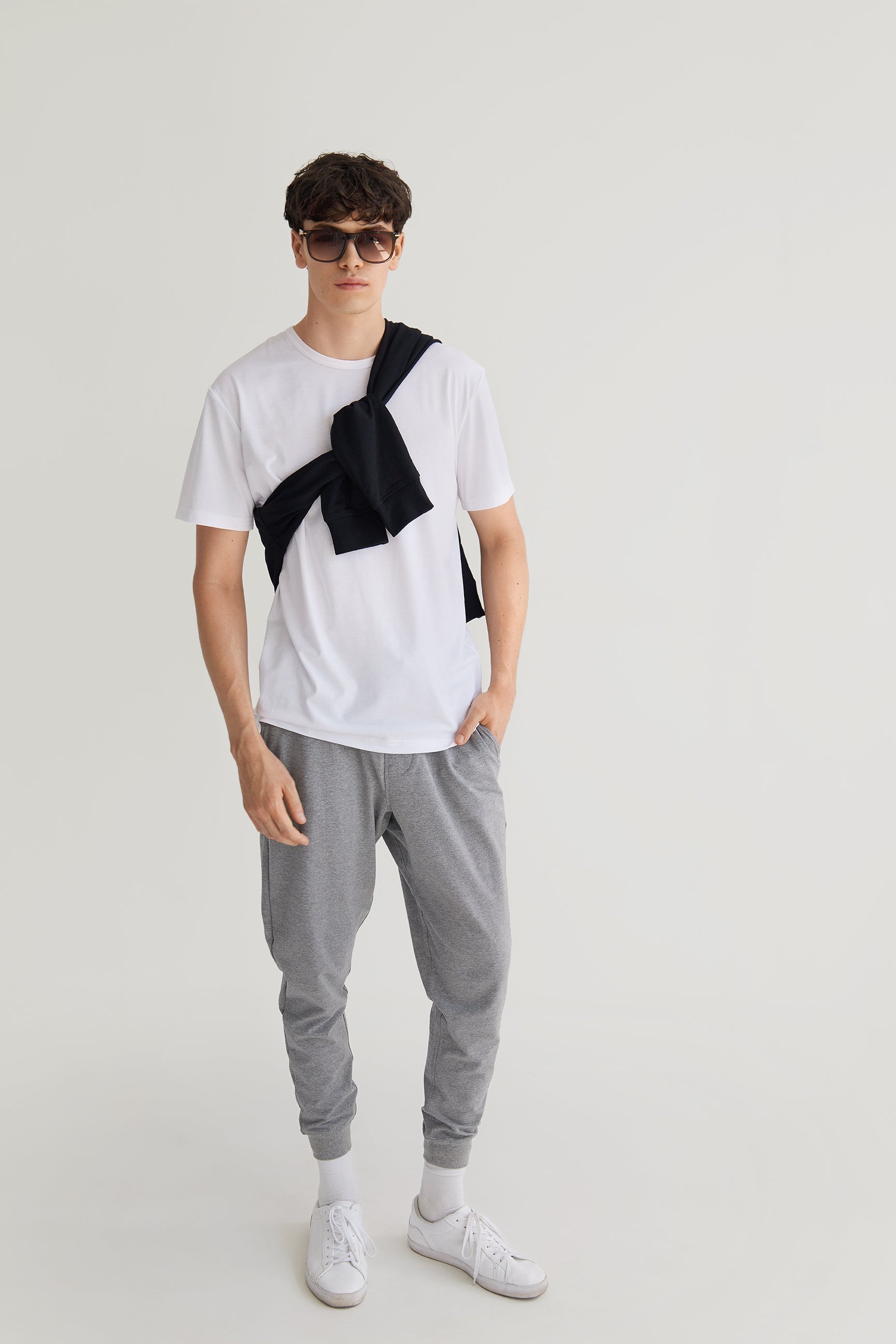 Person wearing a white t-shirt with black suspenders, gray jogger pants, and white sneakers on a light gray background