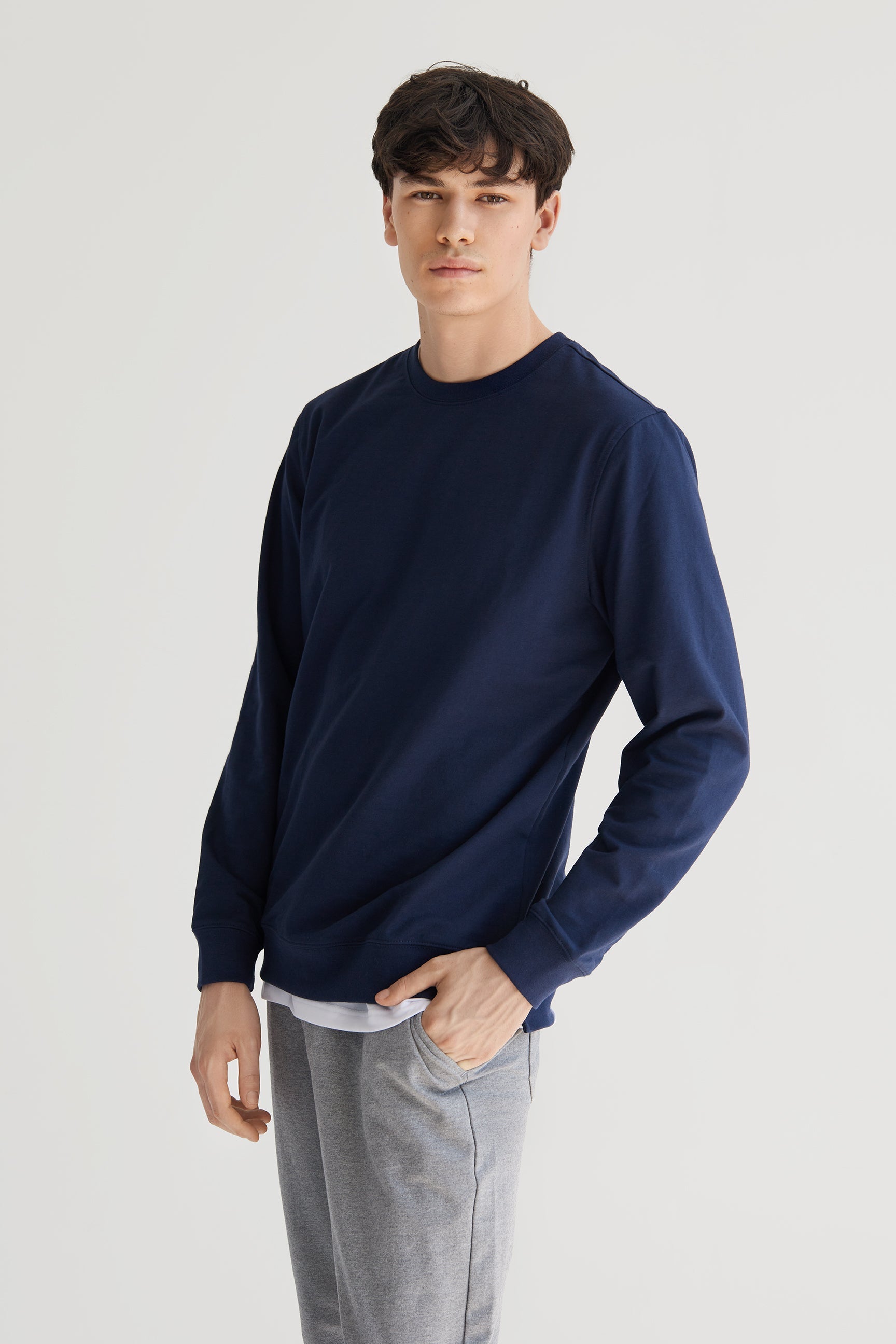 Man wearing a navy blue sweater and gray pants on a light gray background