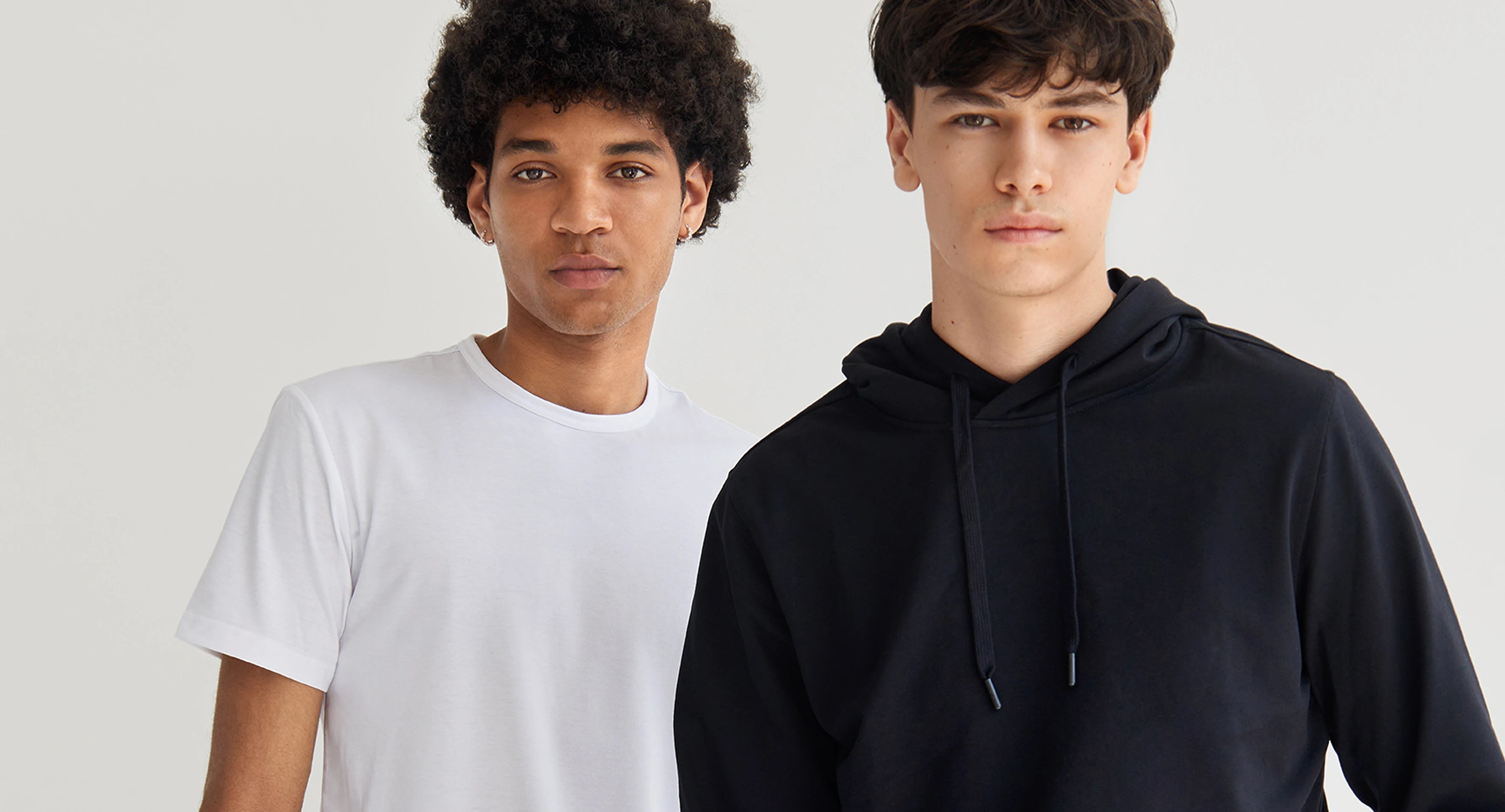 Two individuals wearing a white t-shirt and a black hoodie against a plain background