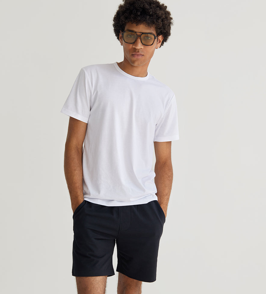 Person wearing a plain white t-shirt and dark shorts on a light gray background