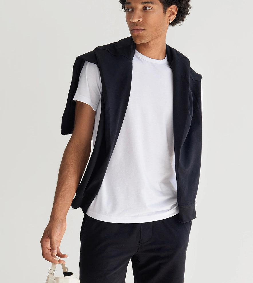 Man wearing a black vest over a white shirt with a plain background