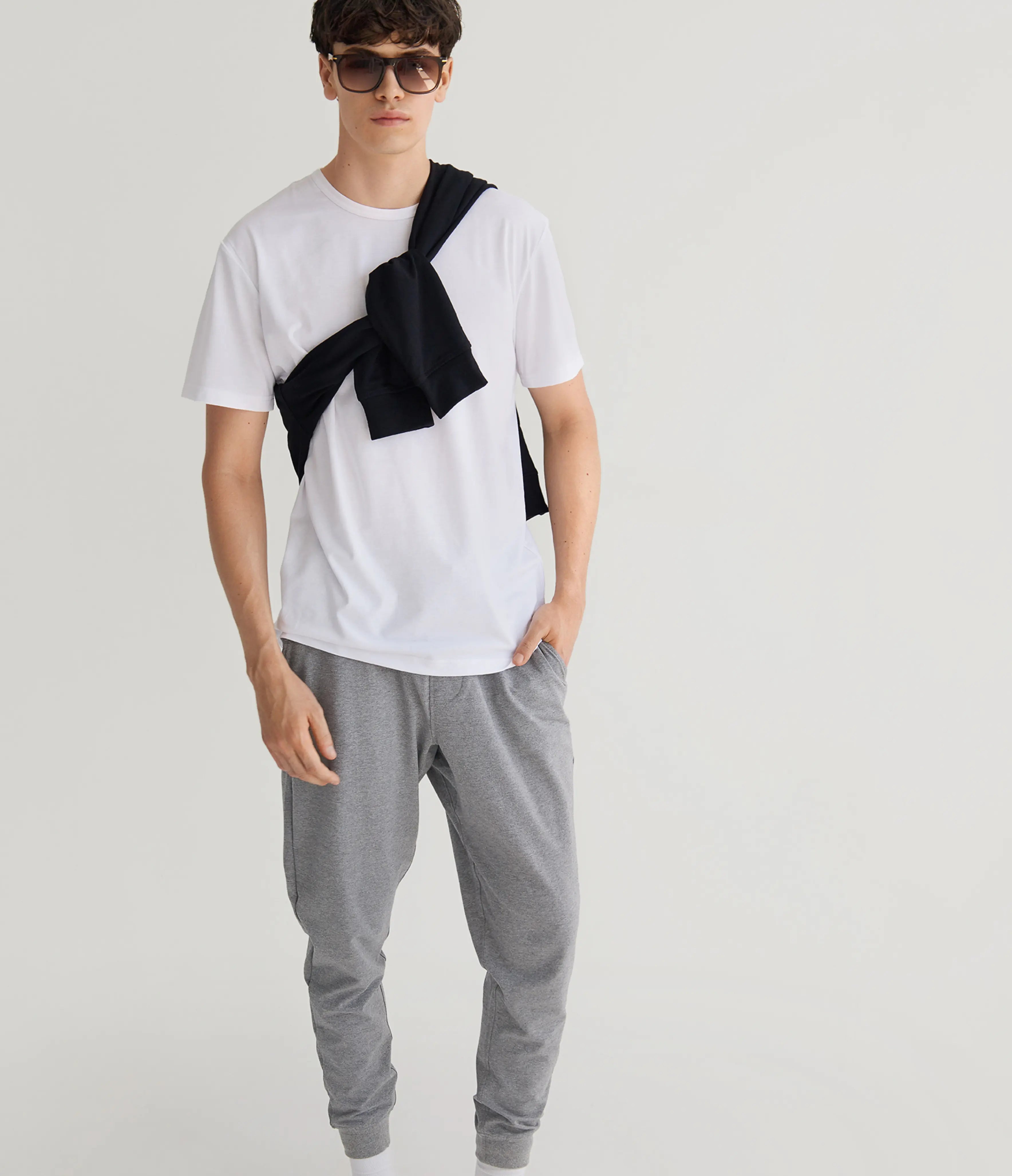 Person wearing a white t-shirt with black accents and gray pants on a light gray background