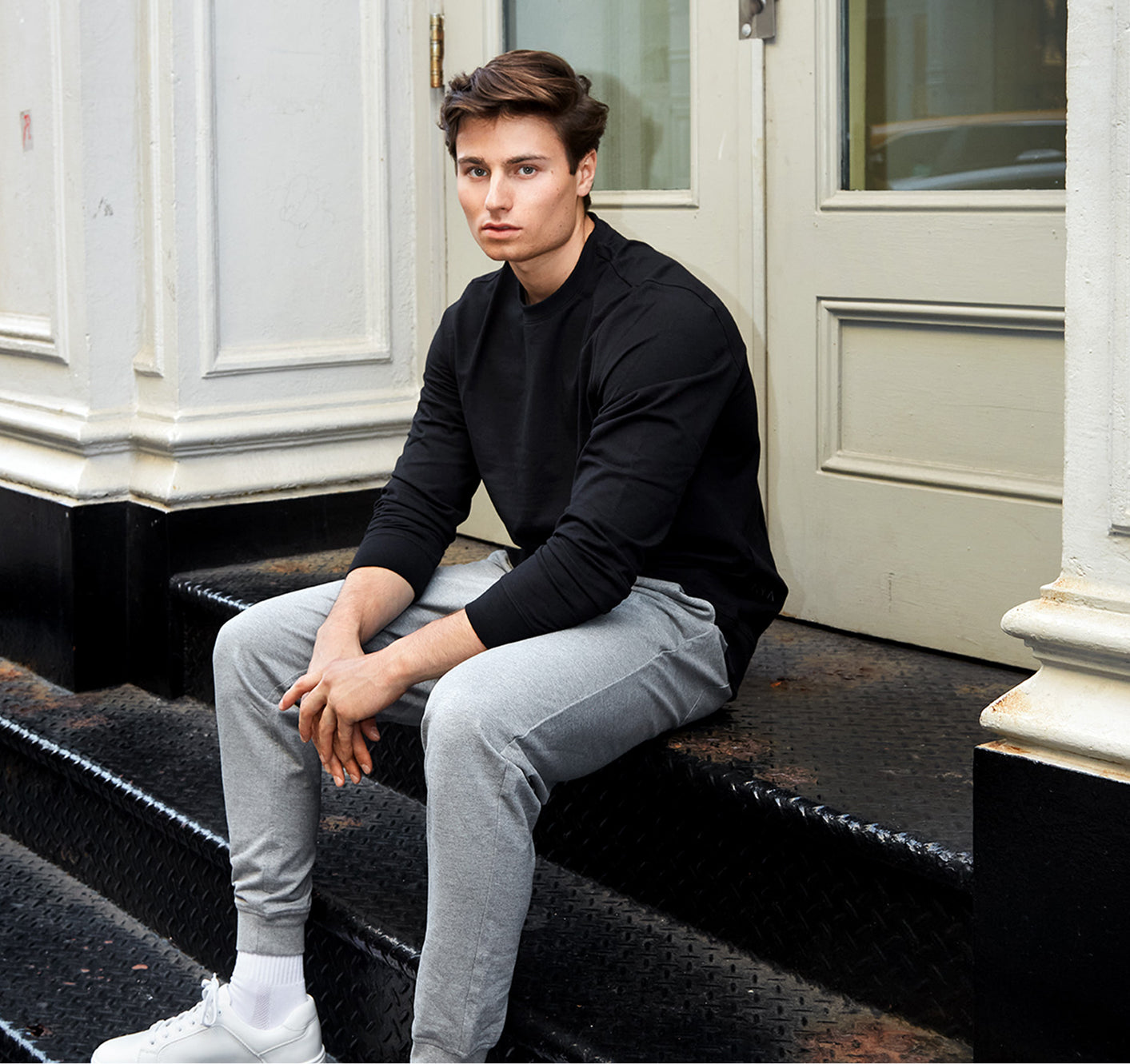 Person sitting on steps wearing a black sweater and gray pants.