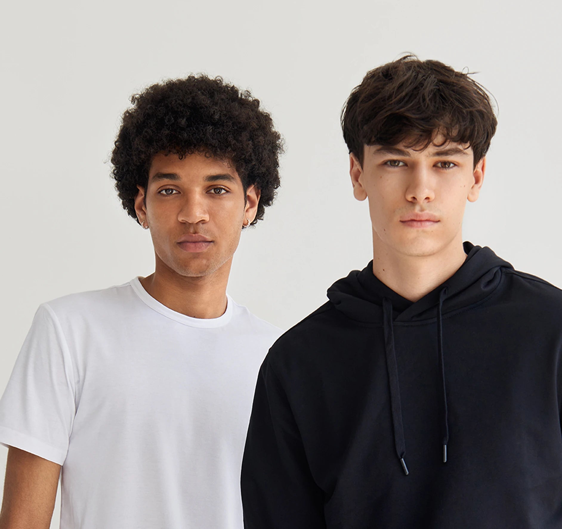 Two individuals wearing a white t-shirt and a black hoodie against a plain background