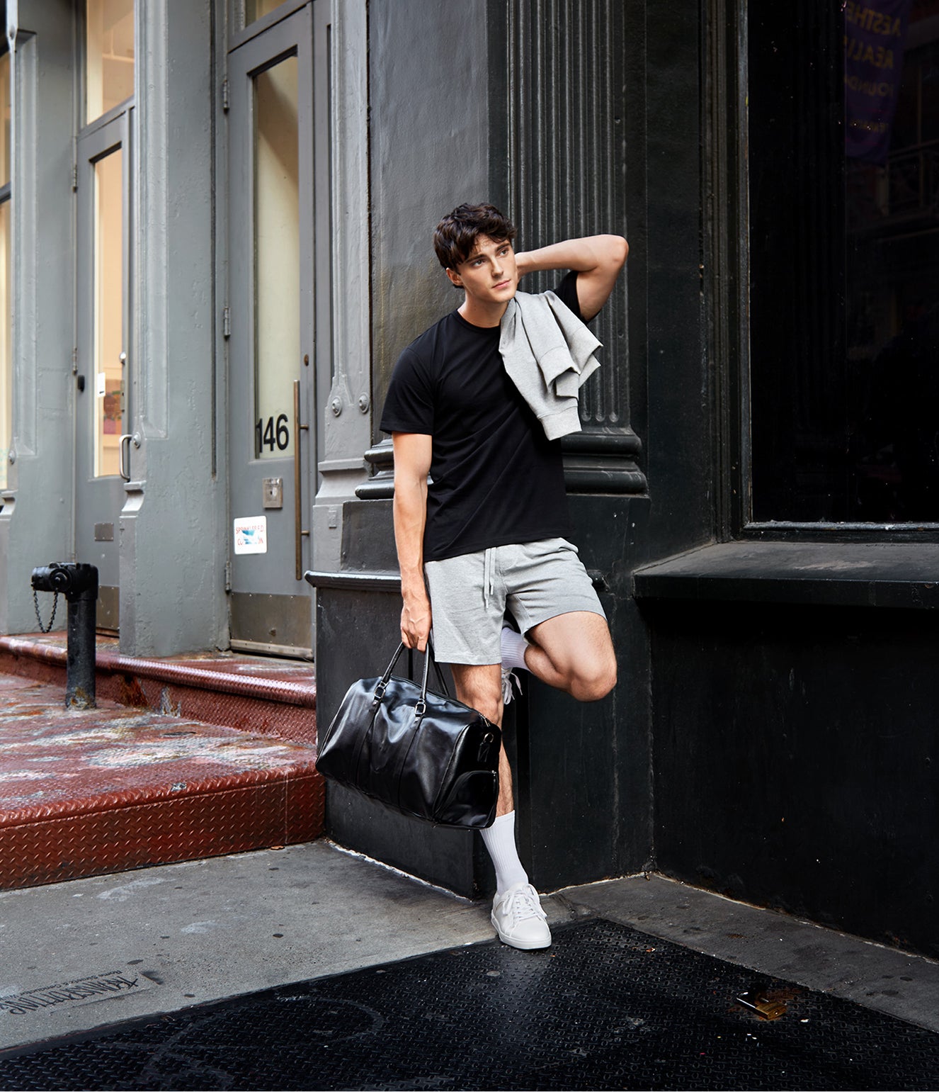 Man in black t-shirt and light shorts holding a black bag on a city street.