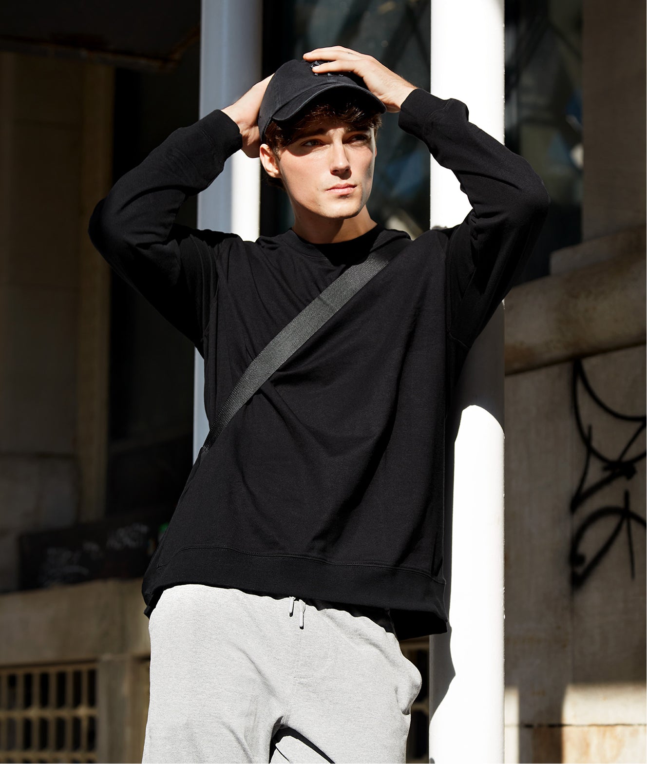 Person wearing a black hoodie and gray pants with a cap, standing outdoors.