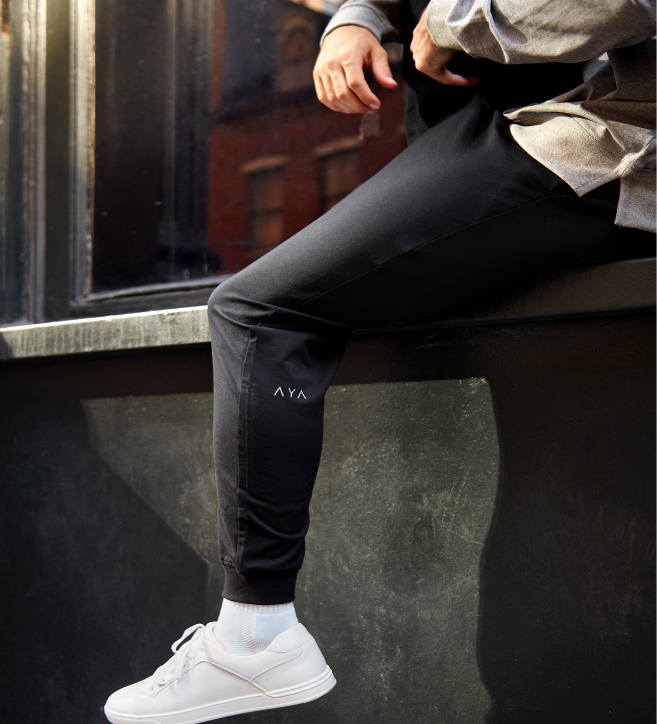 Person wearing black pants with a logo sitting on a bench.