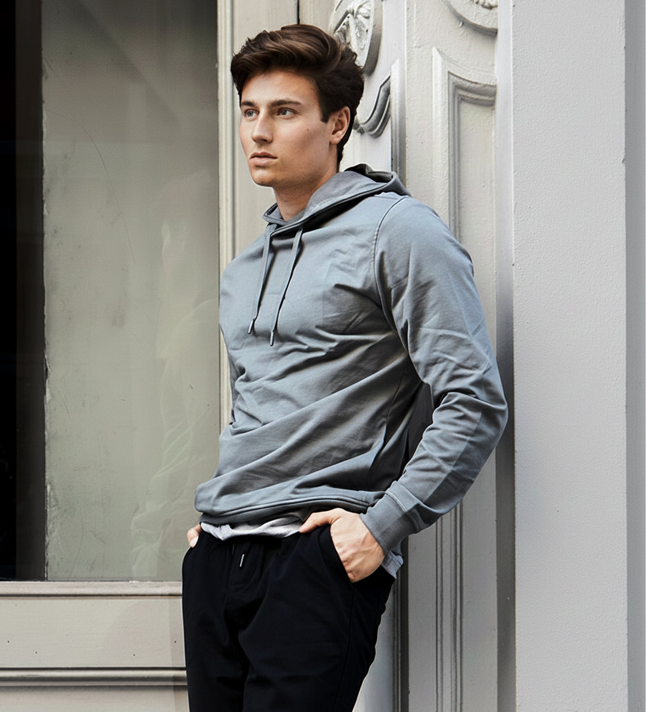 Man wearing a gray hoodie standing against a building.