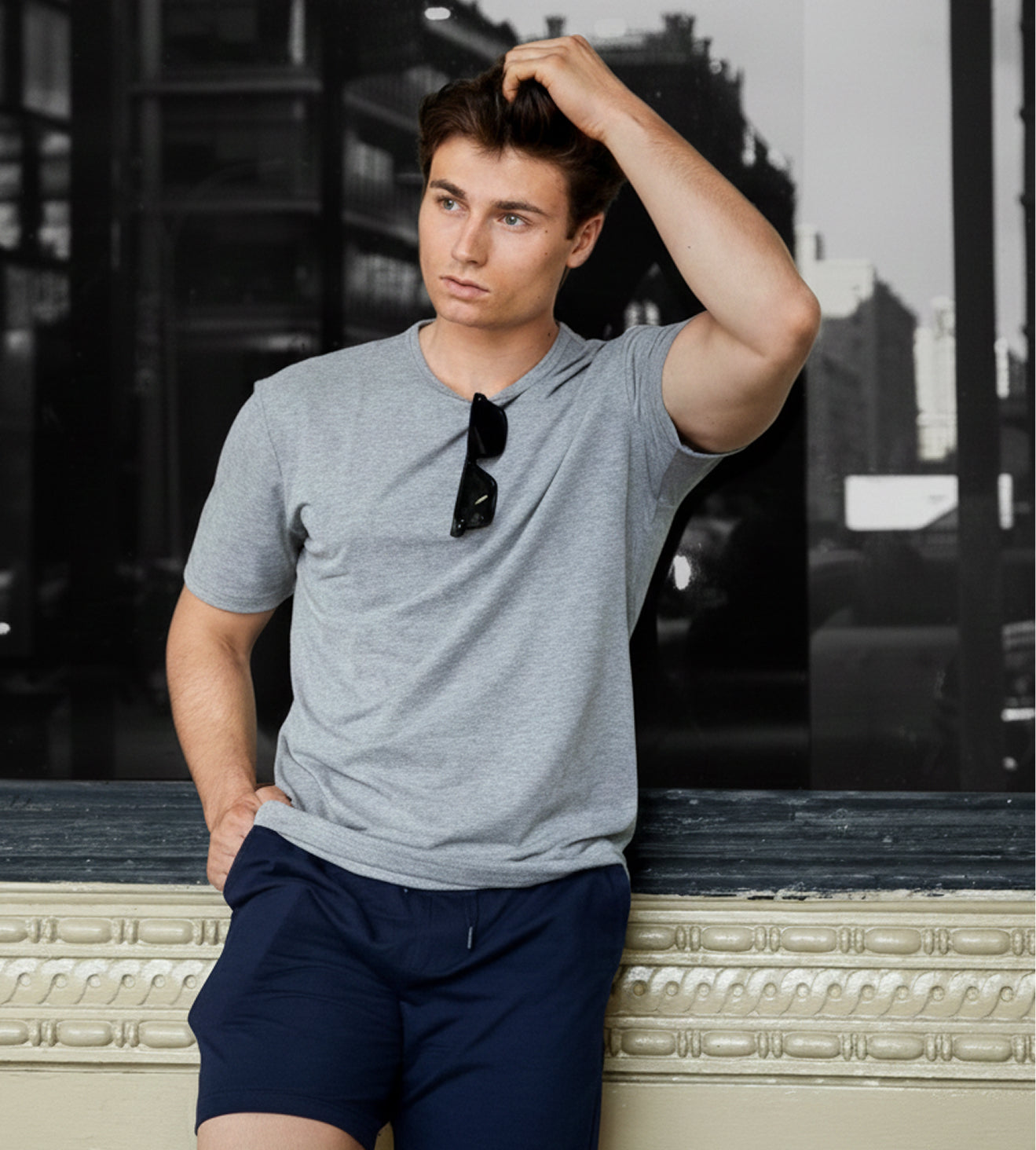 Man in gray t-shirt and navy shorts posing against a blurred urban background