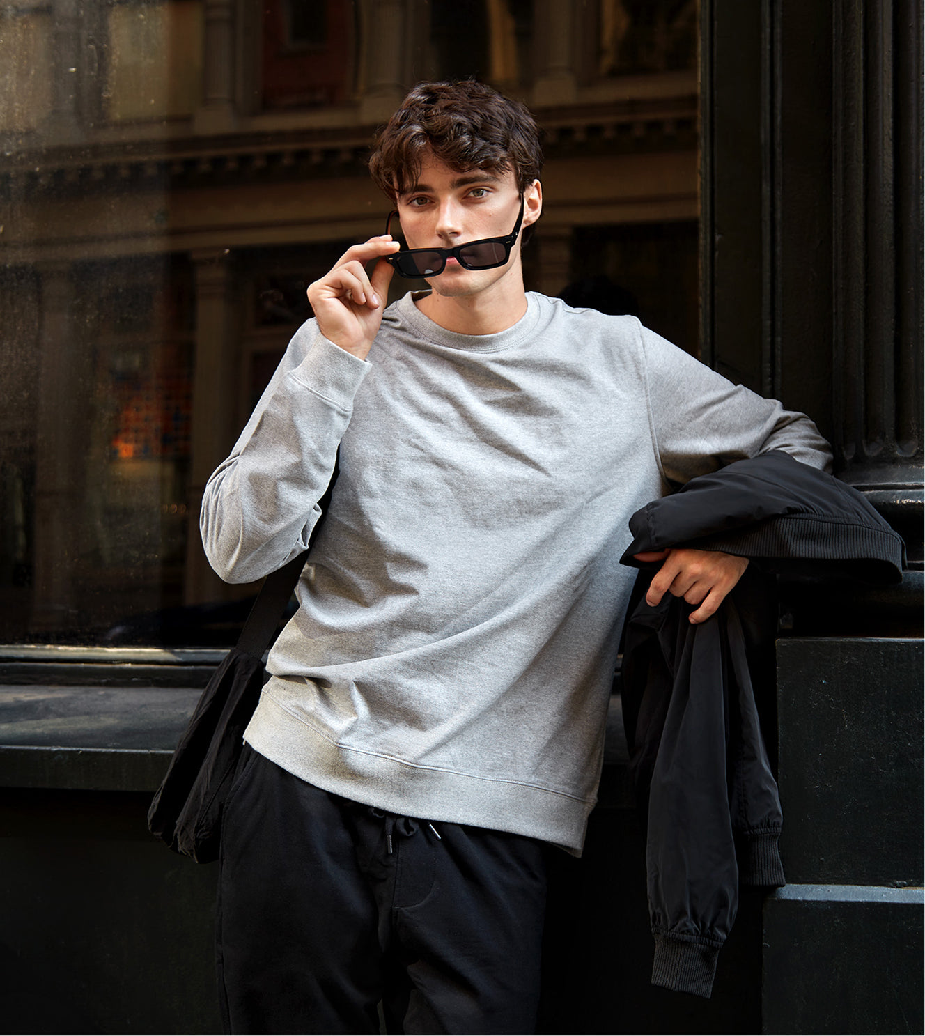 Man wearing a gray sweatshirt and black pants sitting on steps with a dark background