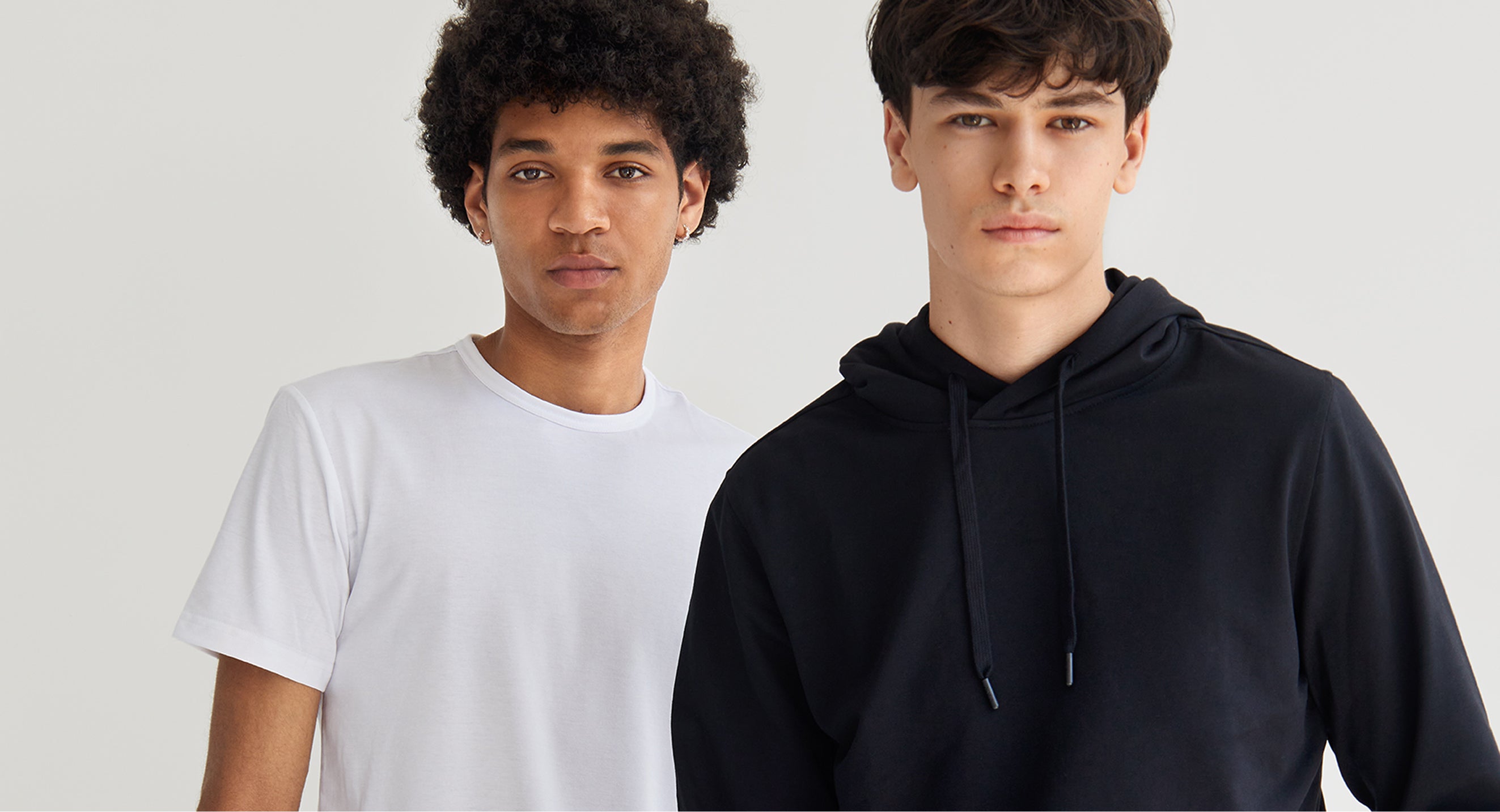 Two individuals wearing a white t-shirt and a black hoodie against a plain background